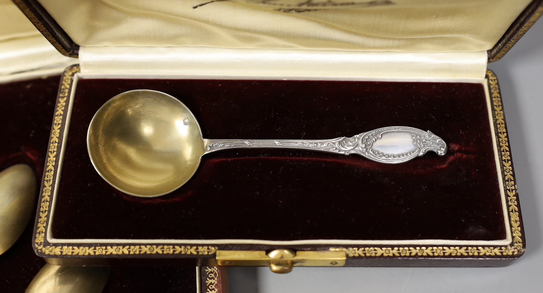 A cased set of twelve early 20th century French white metal fancy pattern teaspoons, a similar cased preserve spoon and a similar cased pair of white metal handled grape shears.